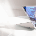 A laptop with a touchscreen displays colorful graphs and data visualizations on a white table in a bright environment.