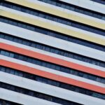 Diagonal stripes in yellow, orange, and red on a white building facade with dark windows.