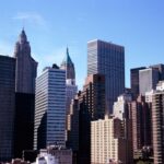 Skyline of tall buildings in a city, featuring a mix of modern and classic architectural styles under a clear blue sky.
