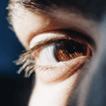 Close-up of a human eye with a brown iris, reflecting light and showing detailed eyelashes.