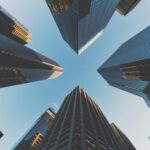View looking up at tall skyscrapers with glass facades against a clear blue sky, creating a star-like pattern.