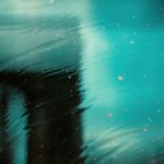 Abstract image with a blurred turquoise background, featuring dark shapes and specks of dirt creating a textured effect.