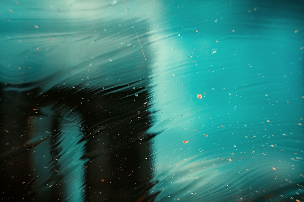 Abstract image with a blurred turquoise background, featuring dark shapes and specks of dirt creating a textured effect.