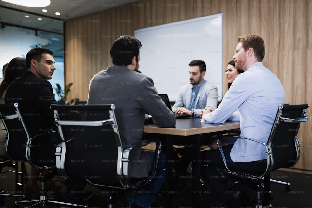 Six professionals engaged in a meeting around a conference table, with a whiteboard in the background.