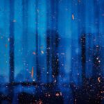 Raindrops and orange particles scattered against a blurred blue background, suggesting a rainy or misty atmosphere.
