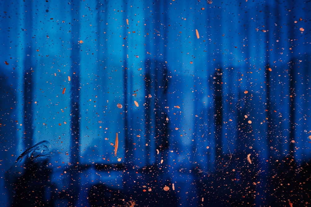 Raindrops and orange particles scattered against a blurred blue background, suggesting a rainy or misty atmosphere.