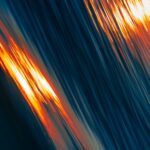 Abstract image of blue waves with streaks of orange light reflecting, creating a dynamic, flowing effect.