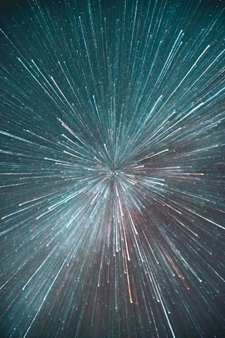 Starry night sky with streaks of light radiating outward, creating a sense of motion and depth in shades of blue and white.