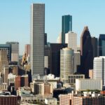 Skyline of Houston, Texas, featuring tall skyscrapers in various styles, with clear blue sky and urban landscape below.