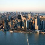 Aerial view of Manhattan, New York City, showcasing skyscrapers, the East River, and the Hudson River at sunset.