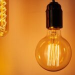Two light bulbs hang against a warm orange background. One is a vintage-style filament bulb, and the other is a long, thin tube bulb.