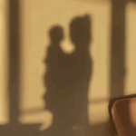 Silhouette of a person holding a child against a wall with golden sunlight streaming through windows.