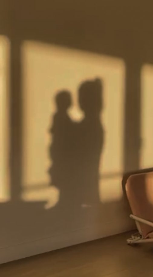 Silhouette of a person holding a child against a wall with golden sunlight streaming through windows.