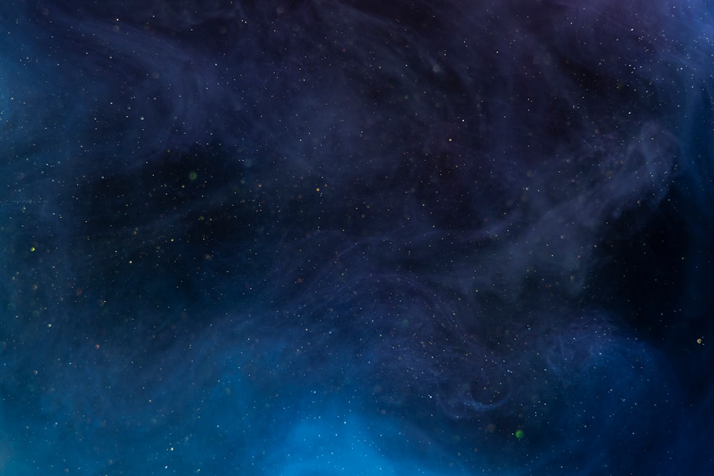 Swirling dark blue and purple cosmic background with scattered stars and faint wisps of light.