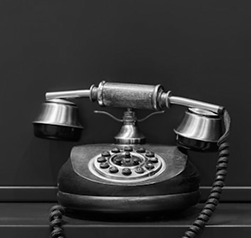 Vintage black rotary telephone with a coiled cord, set against a plain dark background.