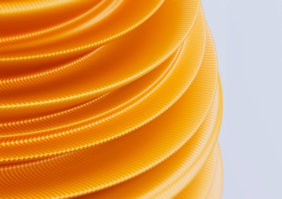 Stacked, wavy layers of bright yellow plastic or rubber, creating a textured spiral pattern against a light background.