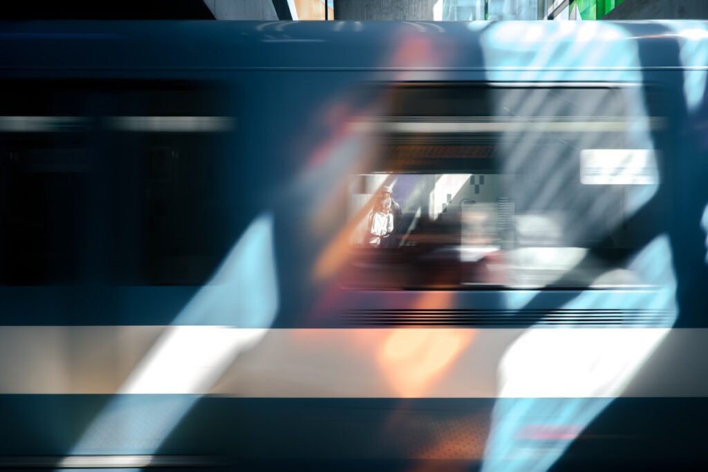 A blurred train moves past with reflections of colorful light; a figure is visible inside one of the windows.