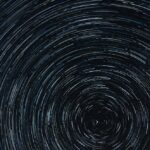 Swirling star trails in a dark night sky, creating circular patterns with varying shades of blue and white.