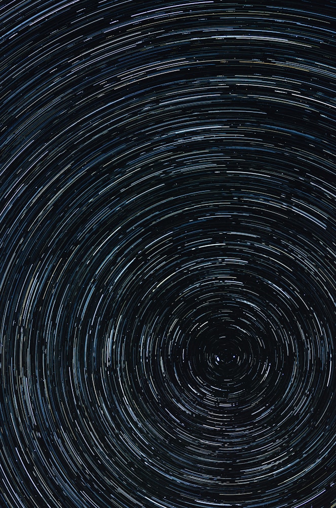 Swirling star trails in a dark night sky, creating circular patterns with varying shades of blue and white.