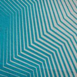 Geometric mural with diagonal white lines on a turquoise background, creating a layered, textured pattern.