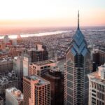 Aerial view of Philadelphia at sunset, featuring the tall, blue-tinted One Liberty Place and city skyline with buildings and the river.