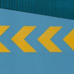 Yellow chevron arrows on a blue wall, arranged diagonally, with a textured green stripe in the upper portion.