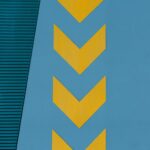 Yellow chevron arrows pointing left on a blue wall, with a textured green panel in the upper portion.