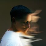 Profile of a person with short dark hair, wearing a white shirt, blurred motion effect creates a sense of movement in the background.