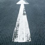 White arrow painted on a textured black asphalt surface, indicating direction forward.