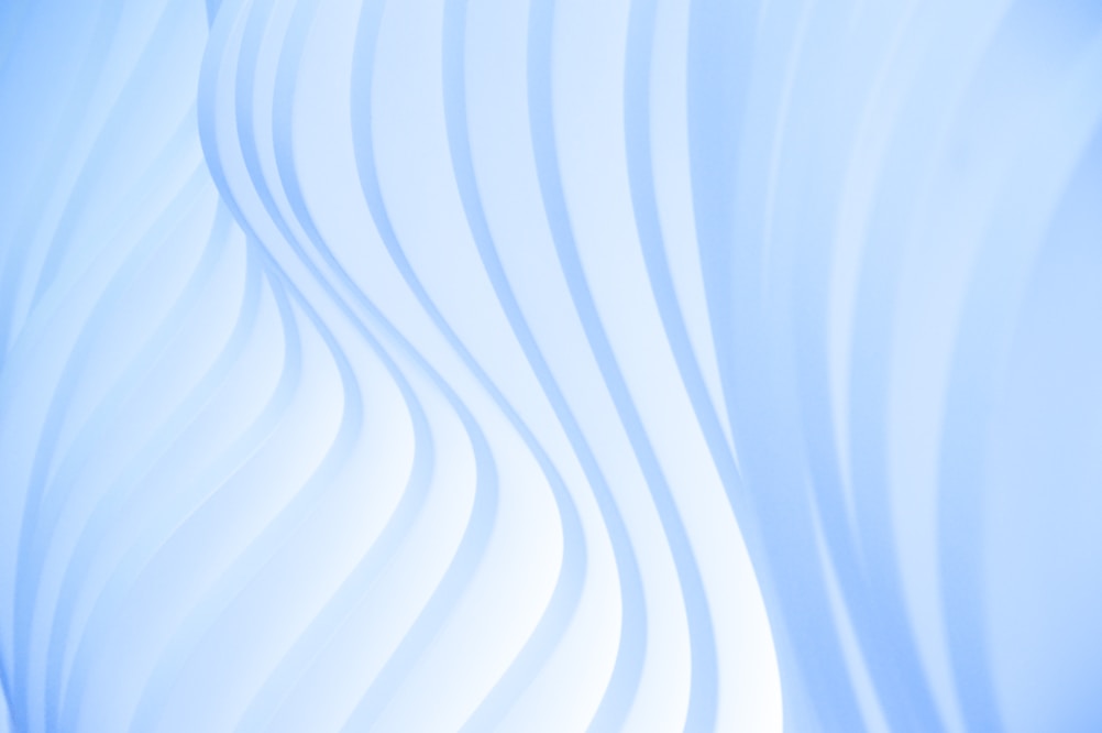 Wavy, translucent white patterns against a light blue background, creating a smooth and flowing texture.