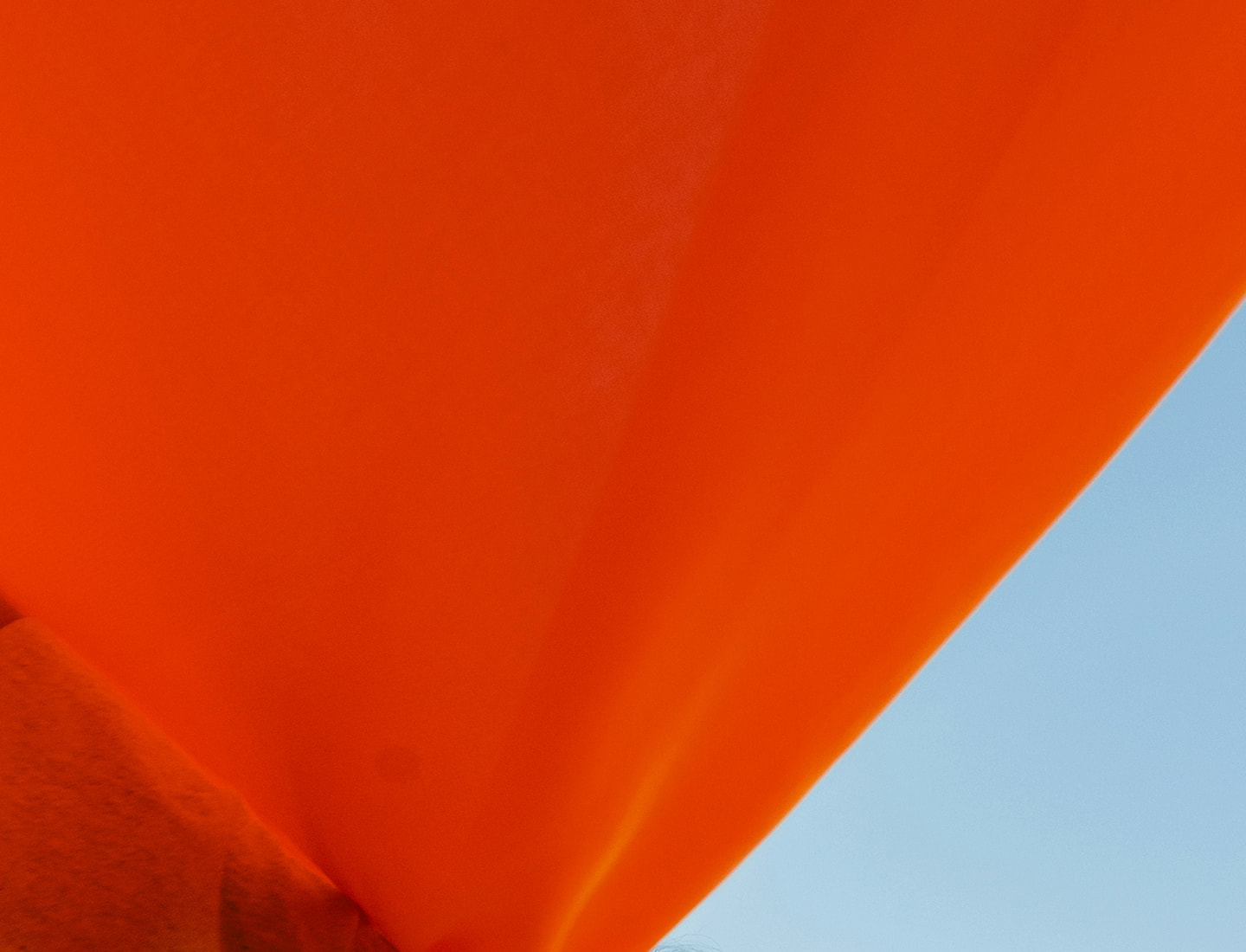 Bright orange fabric drapes diagonally across the image, contrasting with a clear blue sky in the background.