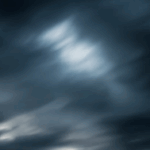 Dark, swirling clouds with varying shades of gray and hints of light peeking through, creating a dramatic sky.