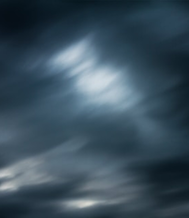Dark, swirling clouds with varying shades of gray and hints of light peeking through, creating a dramatic sky.