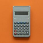 Gray calculator with a digital display, featuring numerical buttons and basic function keys, on an orange background.