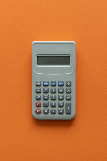 Gray calculator with a digital display, featuring numerical buttons and basic function keys, on an orange background.