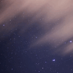 Starry night sky with scattered stars against a dark blue background, partially obscured by wispy clouds.