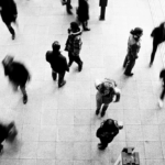 Crowd of people walking in a busy area, captured from above in black and white, with blurred motion.